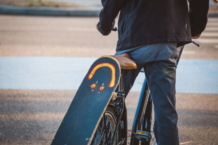Midsection of man with skateboard on bicycle