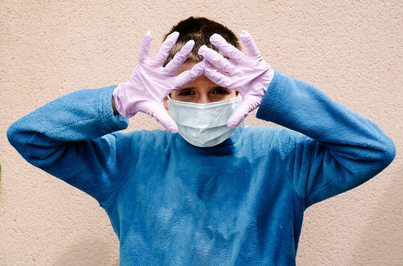 One blonde boy wearing latex gloves and face masks is showing the way he protects himself from coronavirus, bacterias, virus, fungus, etc. he is scared to be infected in pandemic. horizontal