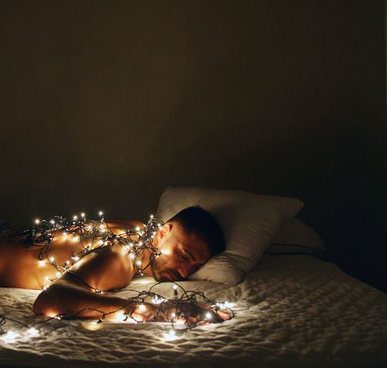 Man sleeping with illuminated string lights on bed at home