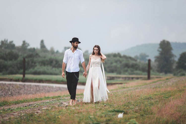 Young couple walking on field against sky