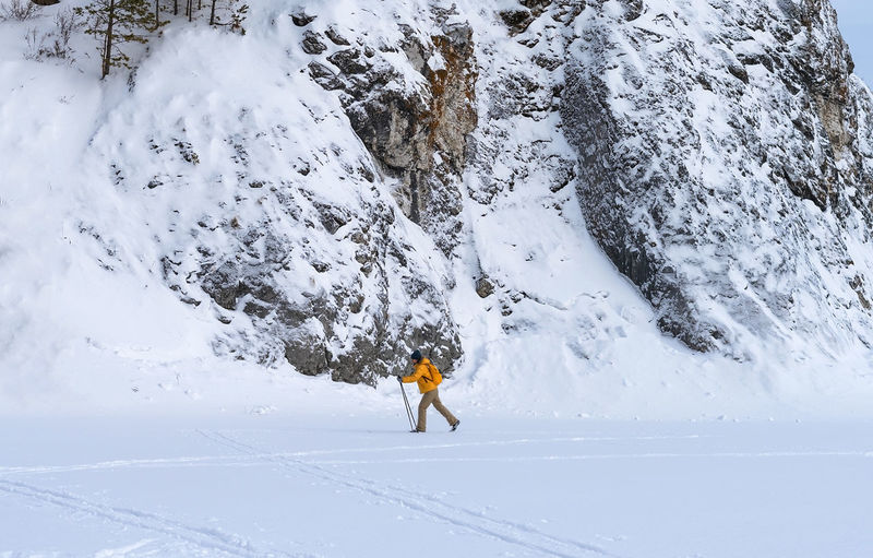 Side view of young woman in yellow clothes with backpack skiing near rocks  winter sports hiking