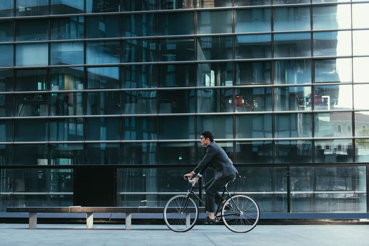 Man riding bicycle on glass building in city