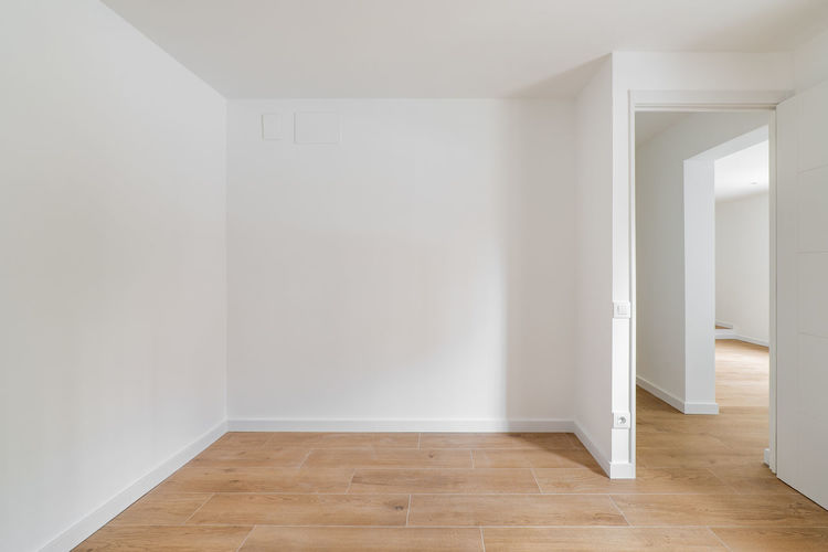 Empty room with laminate flooring and newly painted white wall in refurbished apartment 