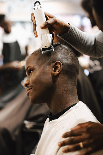 Cropped image of female barber cutting hair of male customer with electric razor at salon