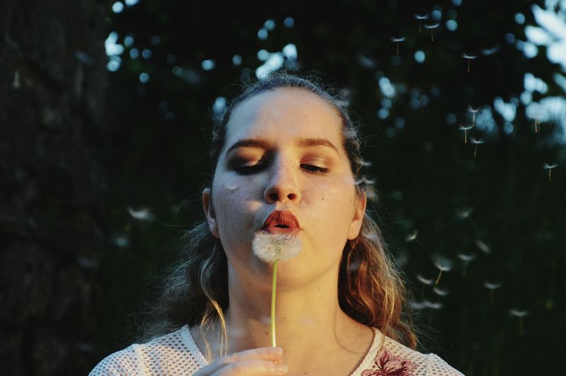 Close-up of young woman blowing dandelion seeds