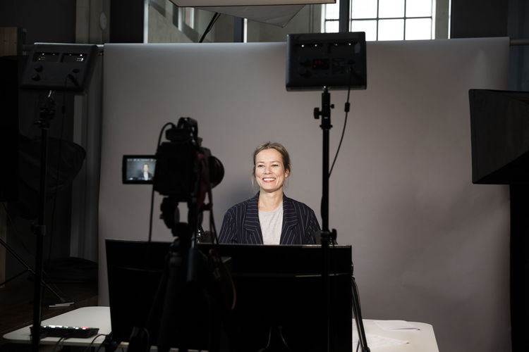 Smiling female entrepreneur video recording on television camera in office