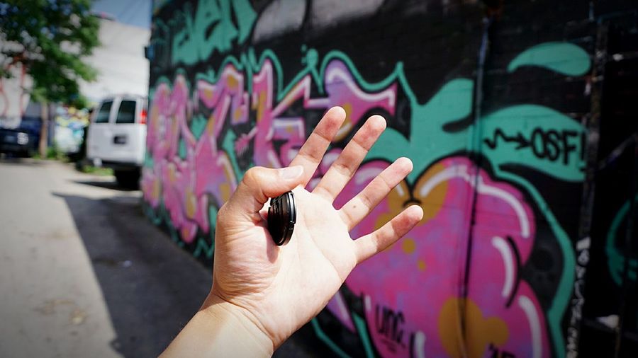 Cropped hand against graffiti wall during sunny day