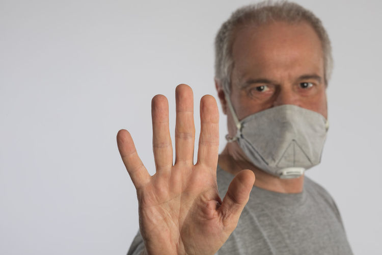 Mature adult wearing a protective face mask and showing the stop gesture with his hand. 