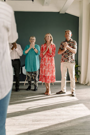 Smiling senior men and women clapping while standing in dance class