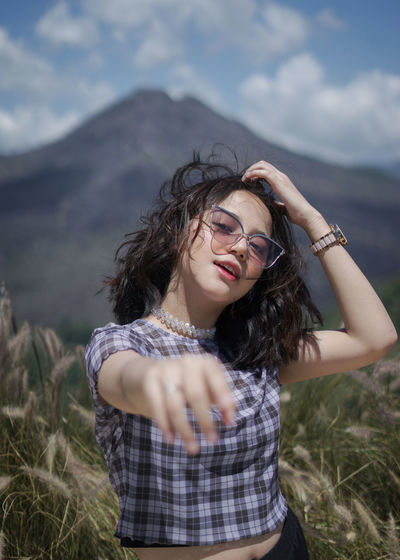 Portrait of beautiful young woman gesturing while standing against mountain