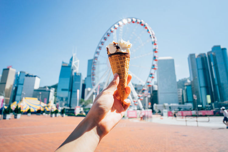 Cropped image of hand holding ice cream against sky