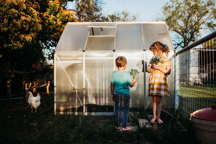 Young kids standing outside backyard green house holding flowers