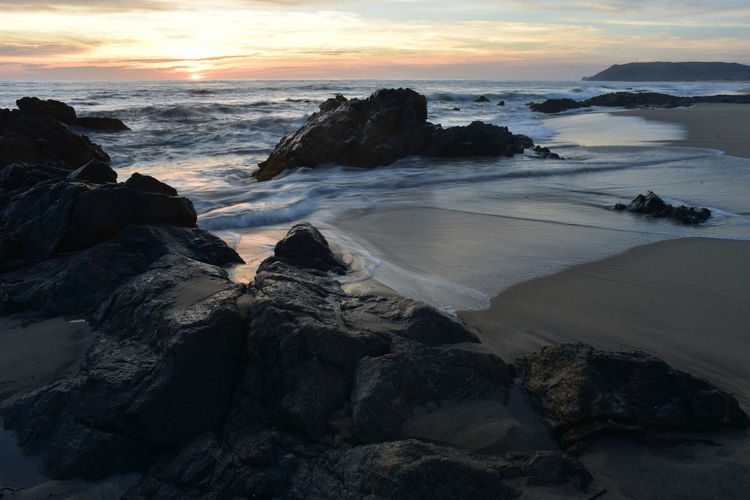 Rocks on beach against sky during sunset