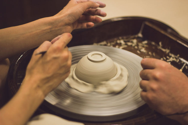 Cropped hands of people working on pottery wheel