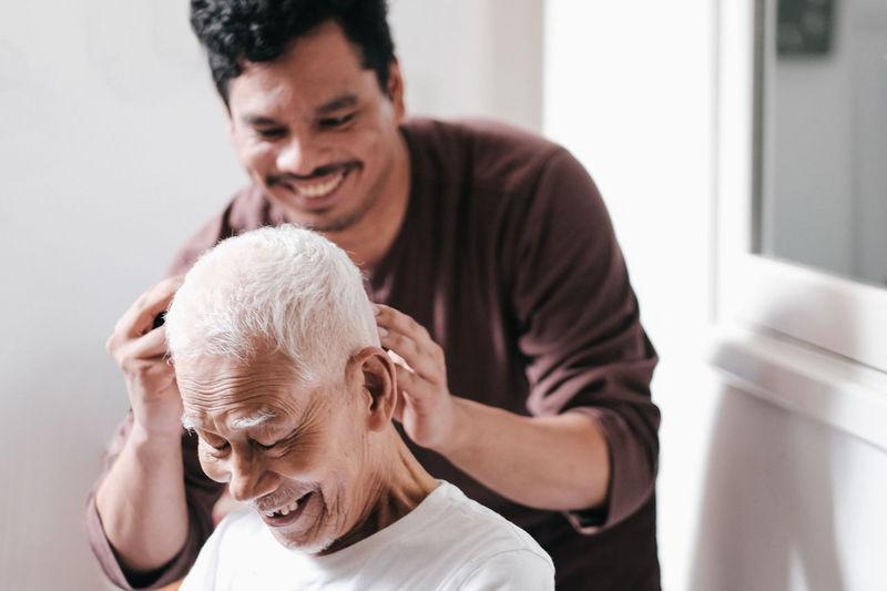 Close-up of smiling grandson cutting senior man hair at home