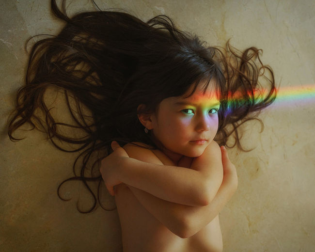 Close-up of young girl laying on the floor with rainbow light falling on her face