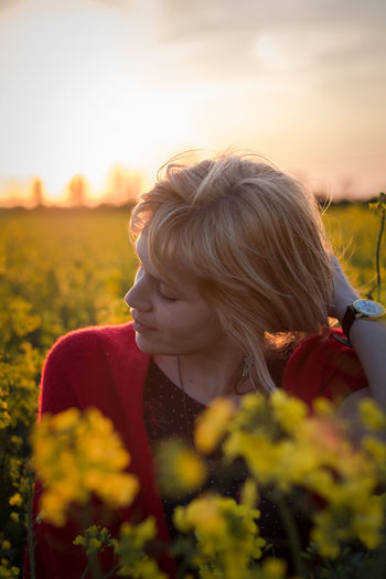 Close-up of woman with hand in hair amidst plants during sunset