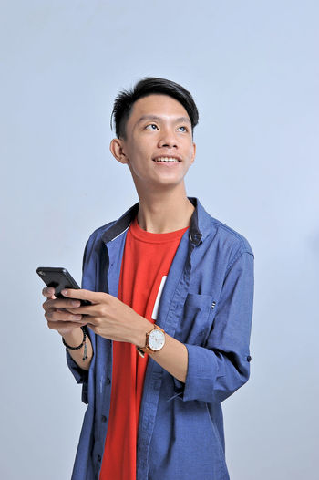 Potrait of handsome young asian man holding a smart phone and wear wristwatch with pretty smiling look at the copy space