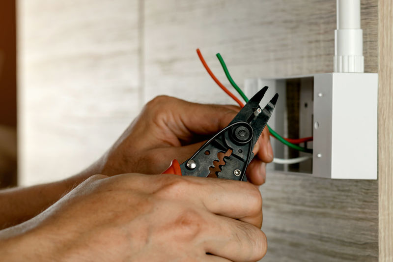 Stripping electrical wires in a plastic box on a wooden wall to install the electrical outlet.