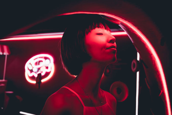 Close-up of young woman standing illuminated red neon light in darkroom