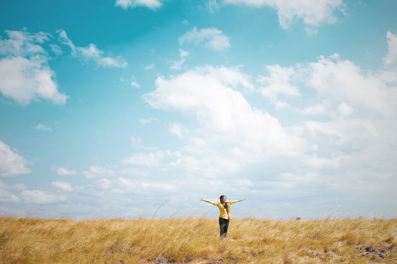 Woman with arms outstretched standing on field against sky