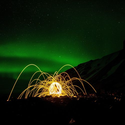 Abstract light painting on field by mountain against aurora borealis