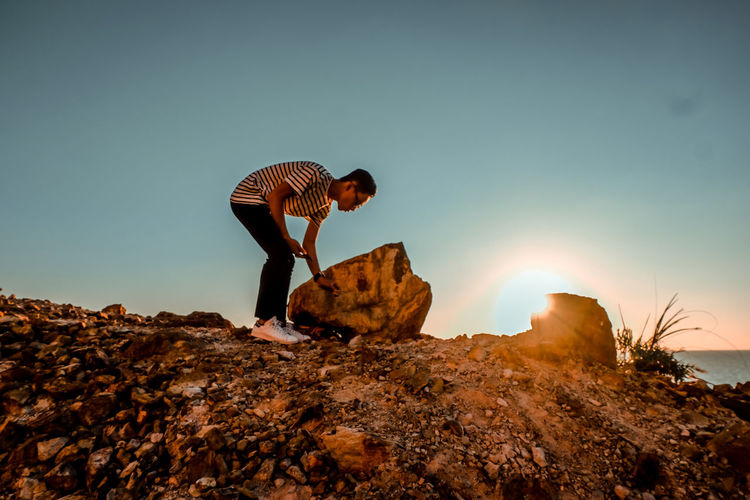 Full length of man standing by rock against sky at sunset