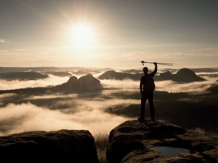 Hiker on peak. tourist man on peak with trekking poles in hand raised in air. marvelous daybreak