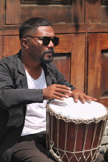 Man wearing sunglasses sitting on the side walk playing drum