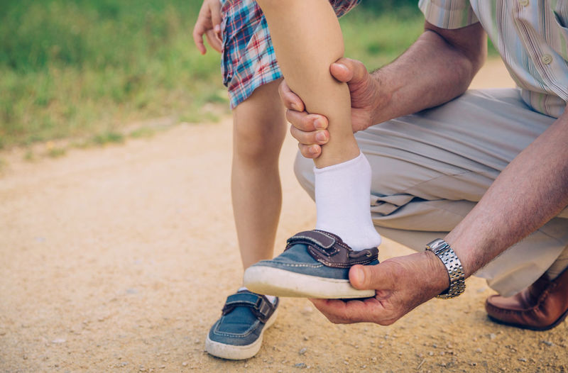 Low section of grandfather helping grandson to put on shoe