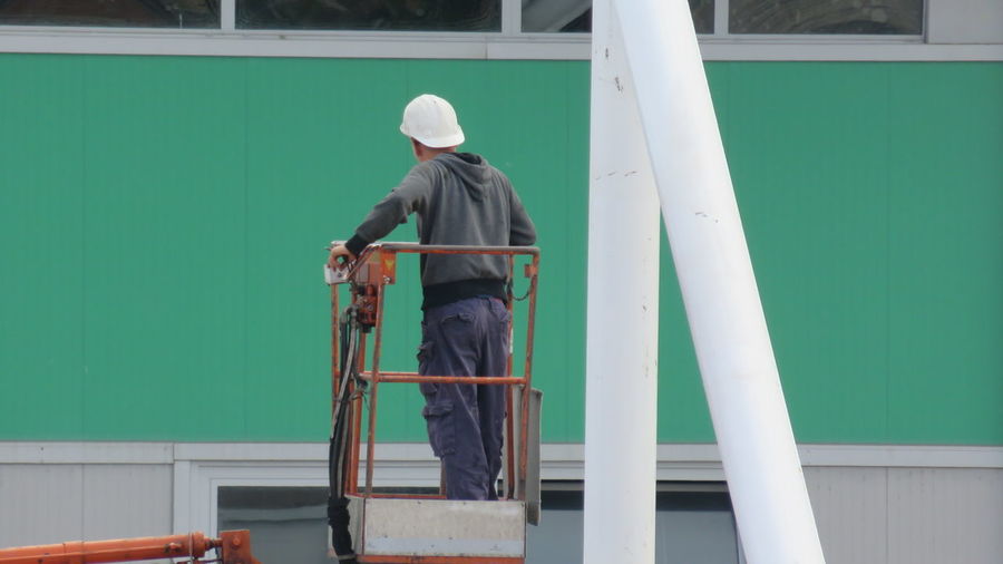 Rear view of construction worker standing on cherry picker against building