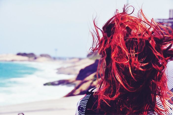 A rear view of a red haired woman walking on a beach