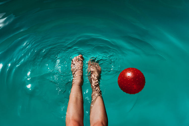 Low section of woman with ball swimming in pool