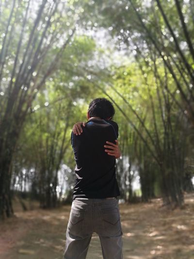 Rear view of man hugging self while standing in forest
