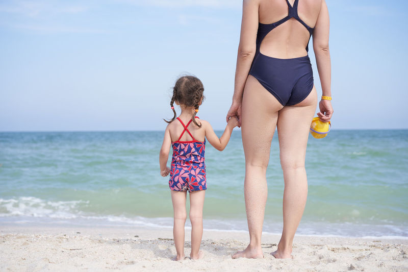 Mother and daughter standing on beach against sky