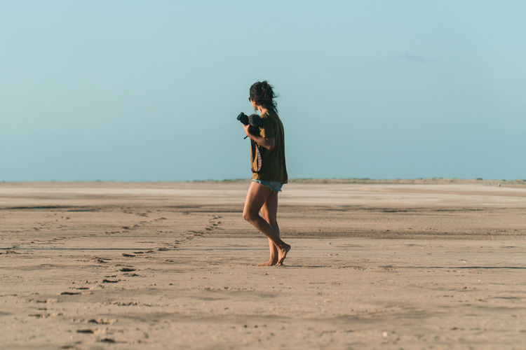Full length of woman walking at beach against clear sky