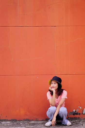 Woman looking away while sitting against orange wall