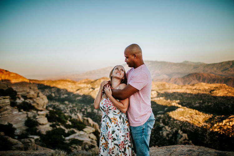 Young couple standing on rock against sky
