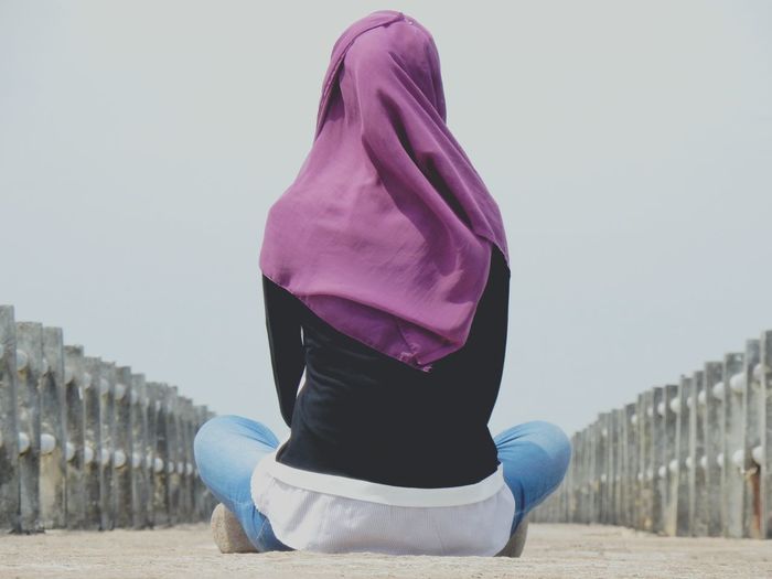 Rear view of woman wearing hijab sitting on bridge against clear sky