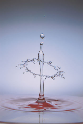 Close-up of drop falling on water against blue background
