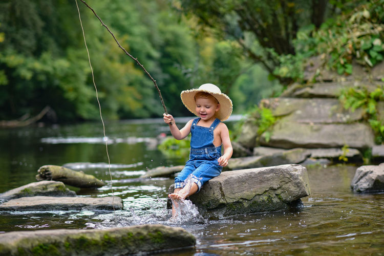 Funny happy little kid fishing at the lake. a fisher boy sits in the lake with a fishing rod