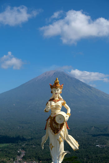Statue against blue sky and volcano