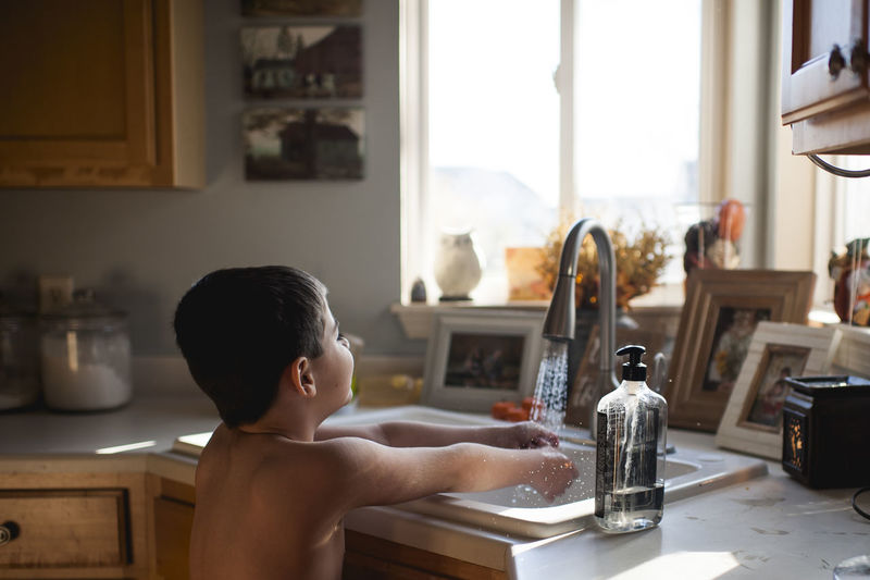 Young boy washes hands in kitchen sink