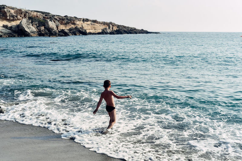 Shirtless boy standing in sea against clear sky