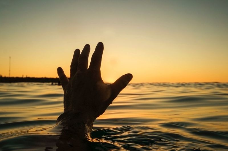Silhouette hand in sea against sky during sunset