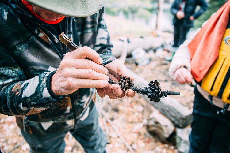 Man plucking pine cone from stick at campsite