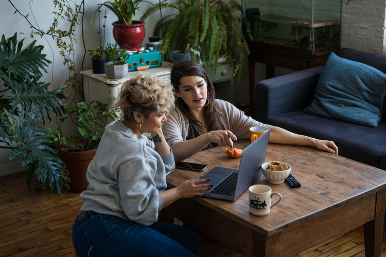 High angle view of woman pointing while friend using laptop at table in living room