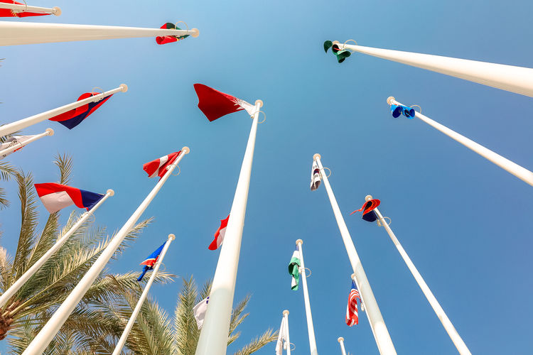 Flags of different countries of world flutters in wind background of blue sky. bottom up view