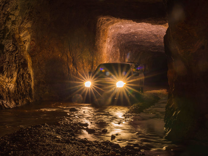 Car lights and flare inside deep old mining tunnel rock cave with reflection. adventure travel.