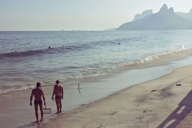 Rear view of shirtless men standing at beach